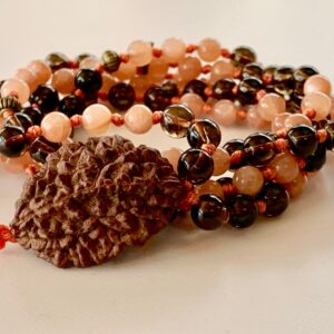 A Sunstone & Smokey Quartz Mala Necklace with 108 hand-knotted beads plus a 2 Mukhi Rudraksha, supporting the Solar Plexus and Root Chakras. Resonates with Leo and Capricorn, promoting vitality, grounding, and spiritual growth. Perfect for meditation and spiritual practice.