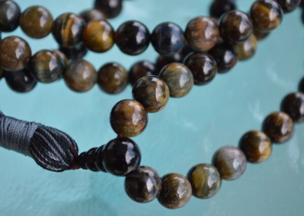 A handcrafted Black Tiger Eye Mala Necklace with 108 beads, designed for strength and protection, resonating with the Root and Solar Plexus Chakras and associated with Capricorn.