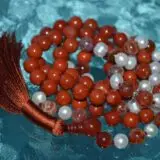 A Red Jasper Mala Necklace with fire agate and pearl beads, featuring 108 mala beads, associated with the Root Chakra, designed for Aries zodiac signs, promoting vitality and courage.