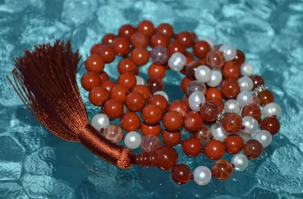 A Red Jasper Mala Necklace with fire agate and pearl beads, featuring 108 mala beads, associated with the Root Chakra, designed for Aries zodiac signs, promoting vitality and courage.