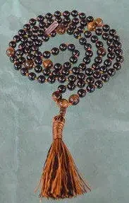 A Black Tourmaline and Tiger Eye Mala Beads Necklace with 108 beads plus 1 guru bead, handcrafted in the USA. Balances the Root and Solar Plexus Chakras, offering protection and courage. Suitable for meditation, spiritual practice, or as a bohemian accessory.