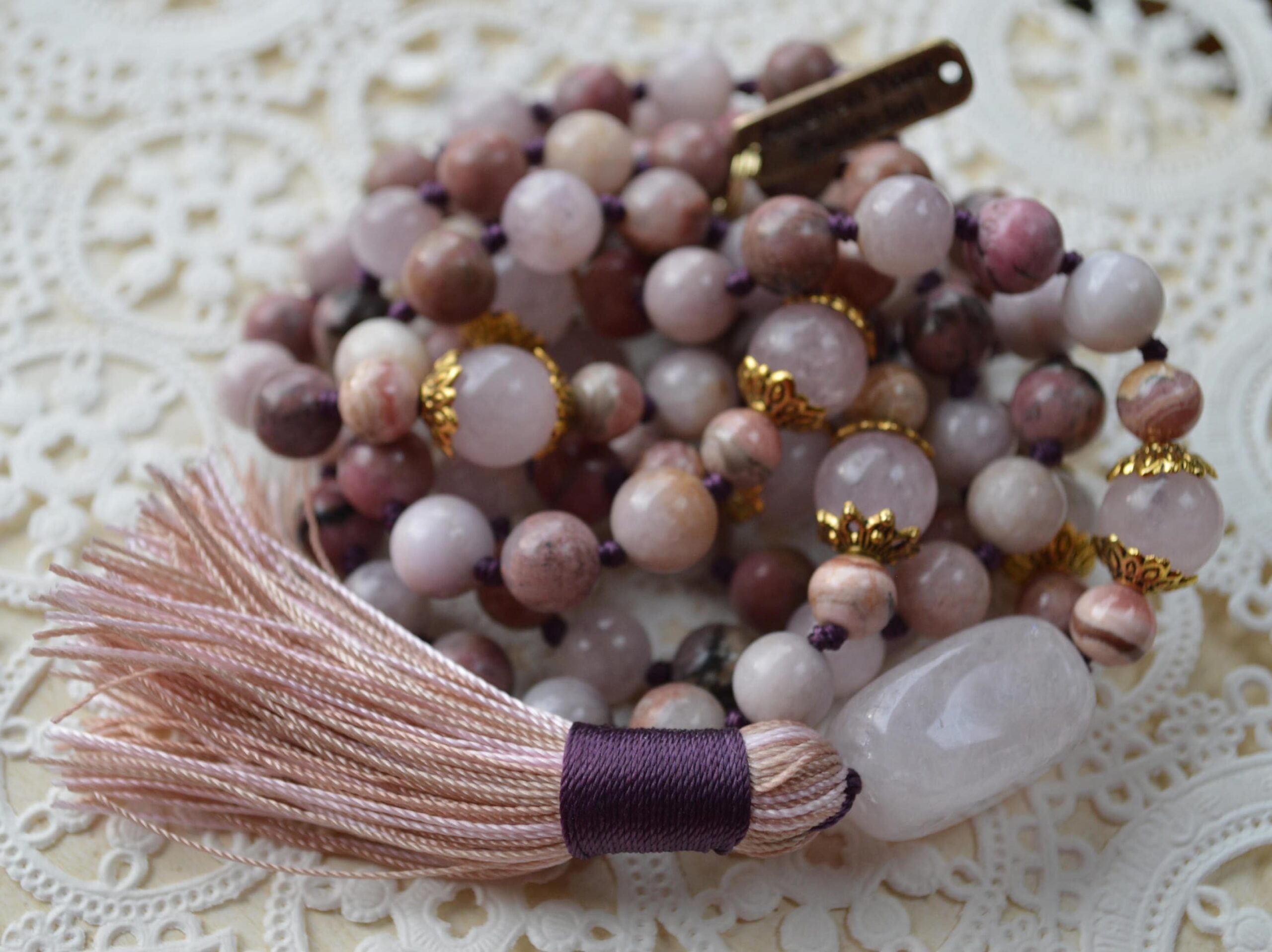 A Kunzite, Rose Quartz, Rhodonite & Rhodochrosite Mala Necklace featuring 108 beads plus 1 guru bead. This necklace supports the Heart Chakra, resonates with Taurus and Libra, and promotes love, compassion, and emotional healing. Hand-knotted and ideal for meditation.