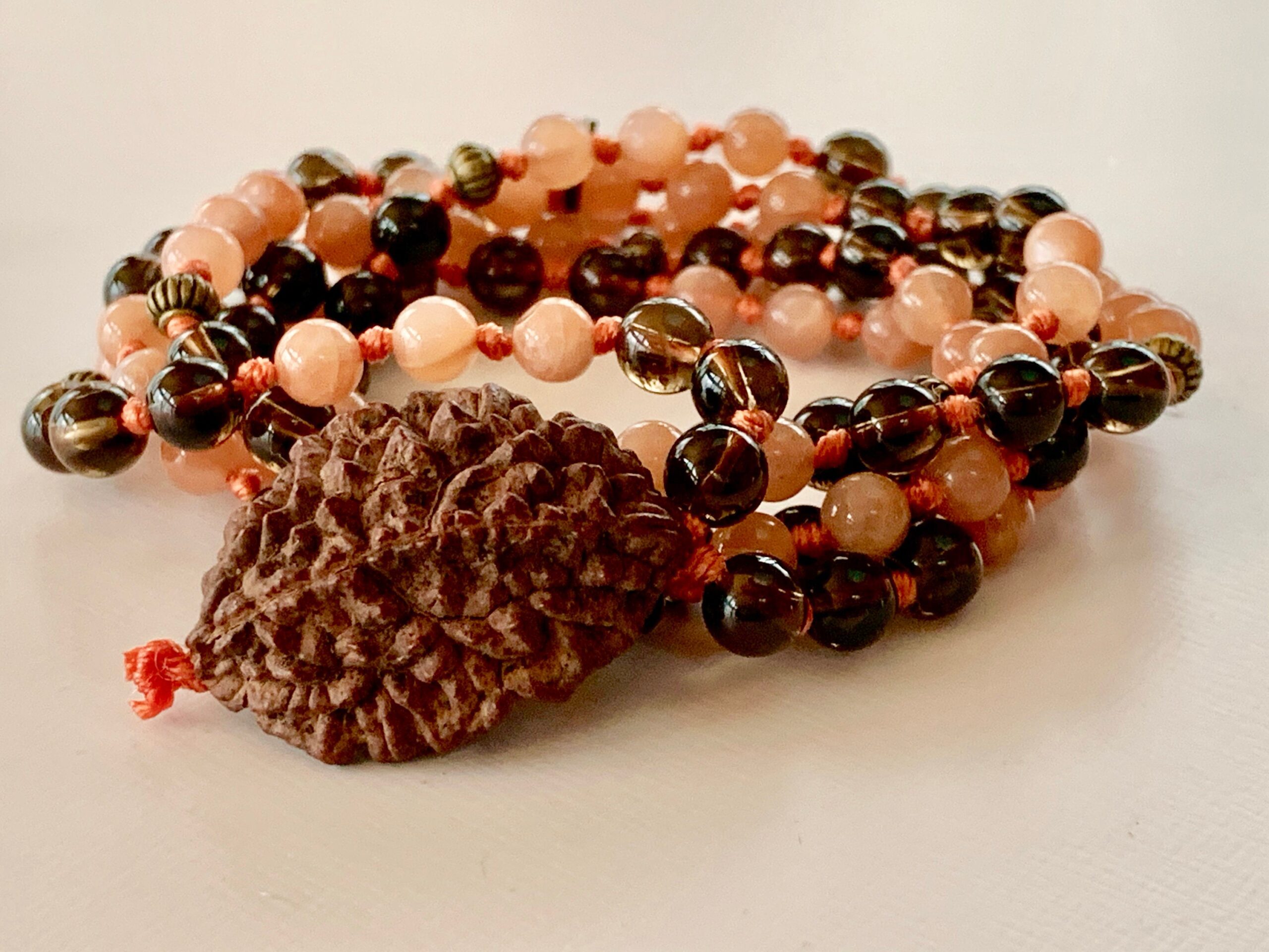 A Sunstone & Smokey Quartz Mala Necklace with 108 hand-knotted beads plus a 2 Mukhi Rudraksha, supporting the Solar Plexus and Root Chakras. Resonates with Leo and Capricorn, promoting vitality, grounding, and spiritual growth. Perfect for meditation and spiritual practice.