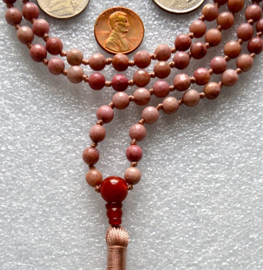 Faceted Rhodonite Mala Necklace with 108 hand-knotted beads, designed to balance the Heart and Root Chakras. Promotes love, compassion, and emotional healing, ideal for Taurus and Leo.